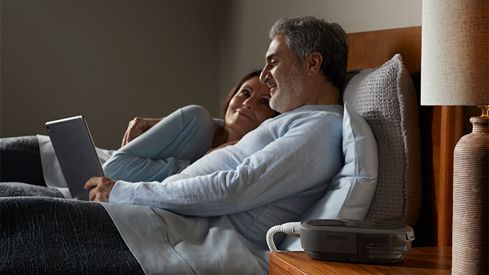 DreamStation 2 Auto CPAP Advanced Couple in Bed with Device on Nightstand
