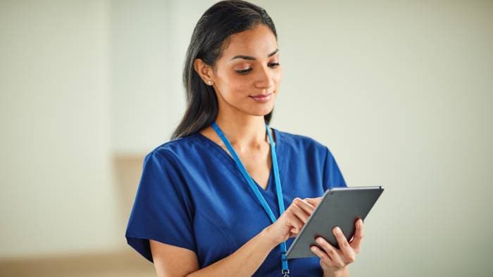 Woman wearing scrubs smiles and works on a tablet.