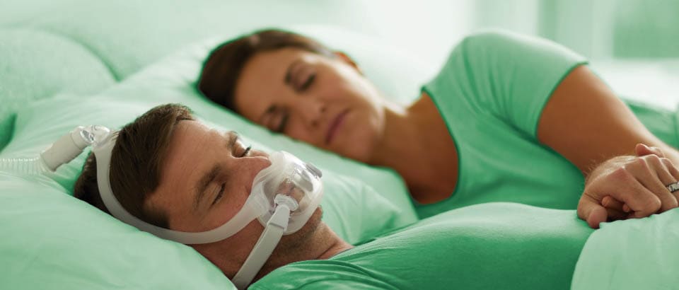 Man in green t-shirt sleeping with a mask and women in green t-shirt sleeping next to him 