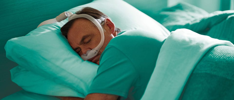 Man in a green t-shirt wearing a mask, sleeping on his stomach