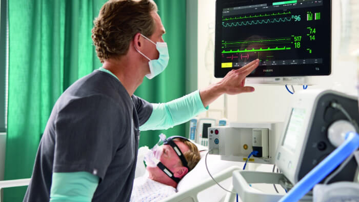 Image of a masked healthcare provider beside the patient, monitoring vitals on a monitor.