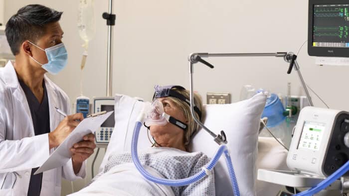 A healthcare provider writes in his notes while reading the monitor above the patient.