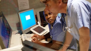 Two health professionals discussing data on a monitor.