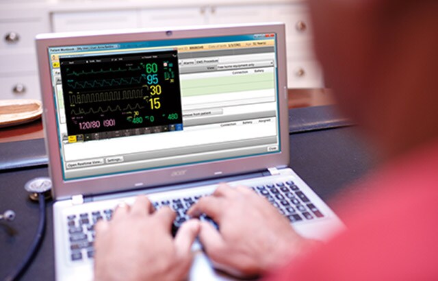 A researcher sits at a desk typing on a laptop showing data on the screen.