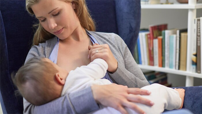 A mother breastfeeds a baby in the cradle hold position.