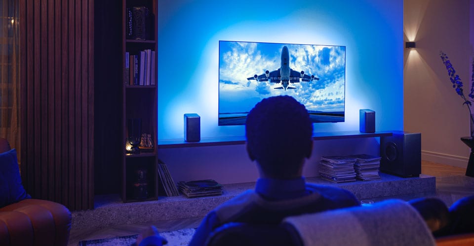 Man enjoying his Philips Ambilight tv connected to wi-fi speakers