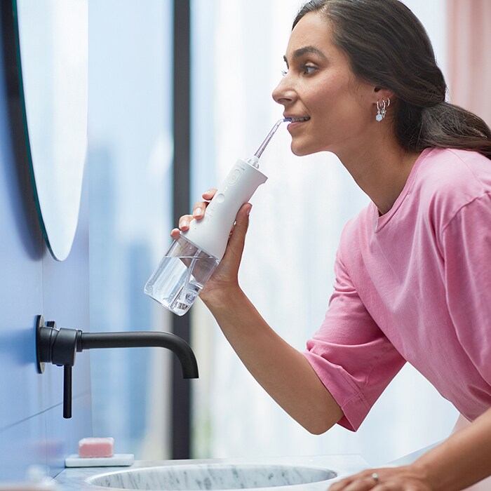 Woman using cordless power flosser by sink