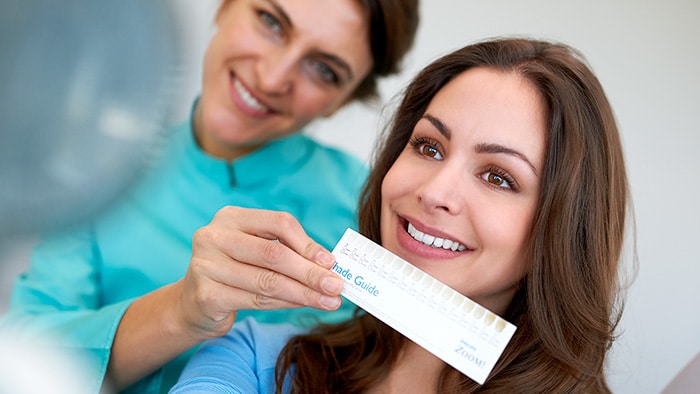A dental professional holding a shade guide below a patient's smile.