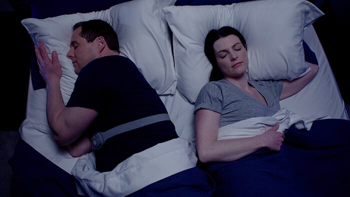Couple sleeping in bed, one is wearing the Snoring Relief Band